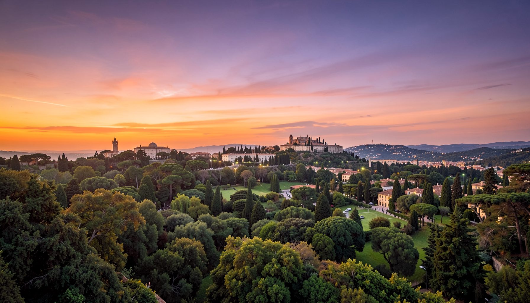 Veduta aerea di un borgo collinare con edifici a cupola e torri tra gli alberi, sotto un cielo aranciato e viola